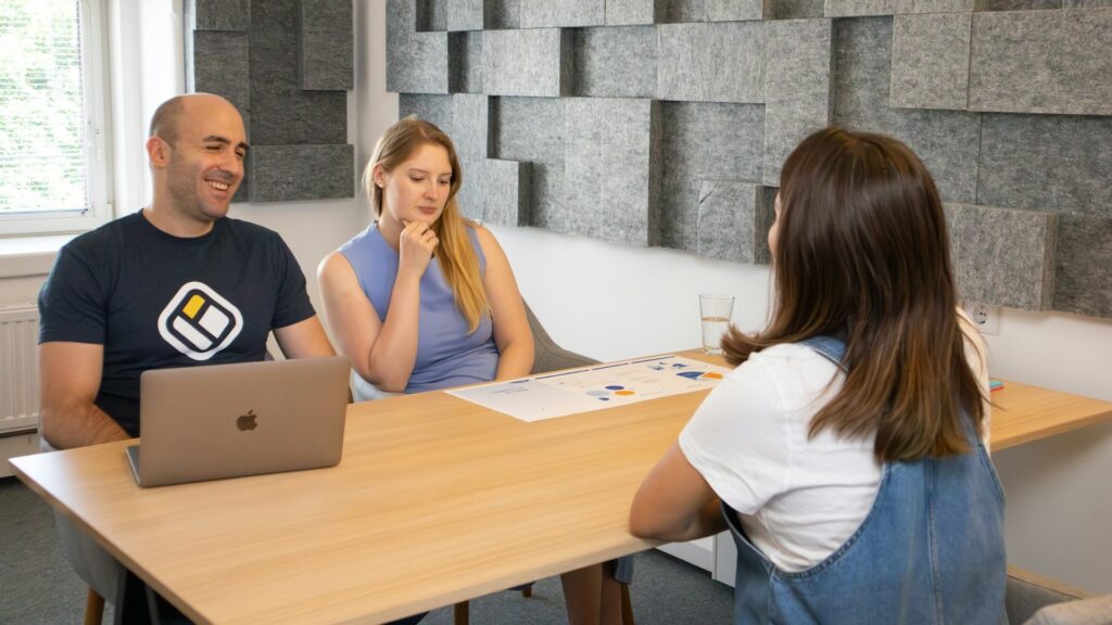 Een vrouw zit tegenover twee interviewers tijdens een sollicitatiegesprek in een moderne kantoorruimte.