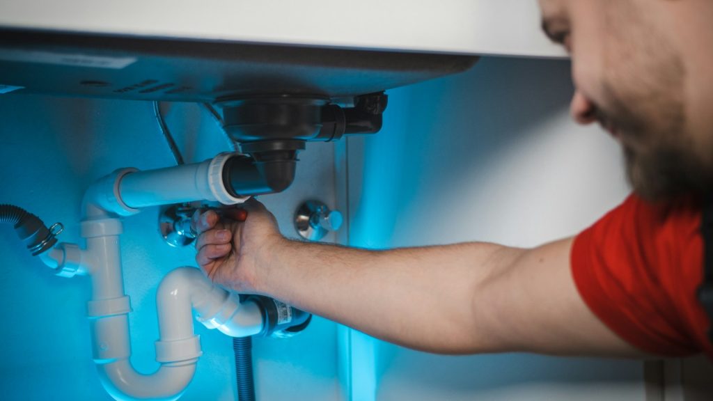 Loodgieter aan het werk onder een gootsteen, belangrijk bij lokaal een specialist kiezen
